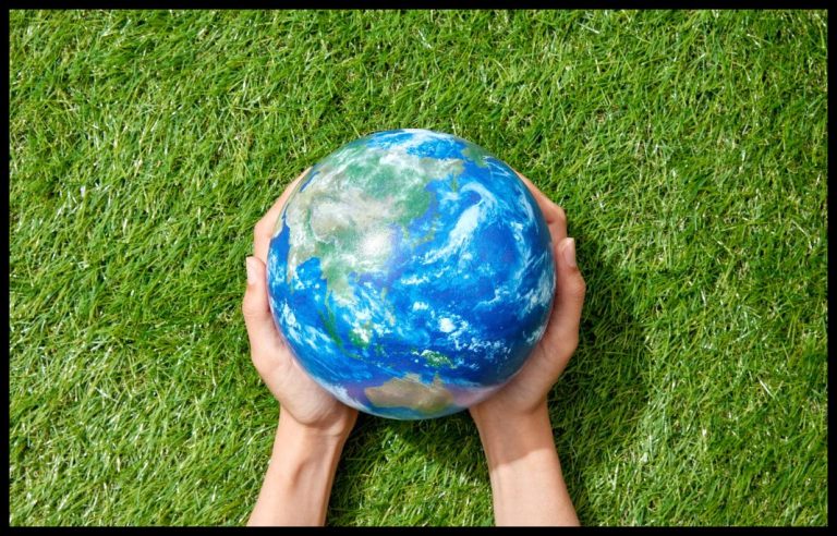 Green grass with persons hands holding a small earth