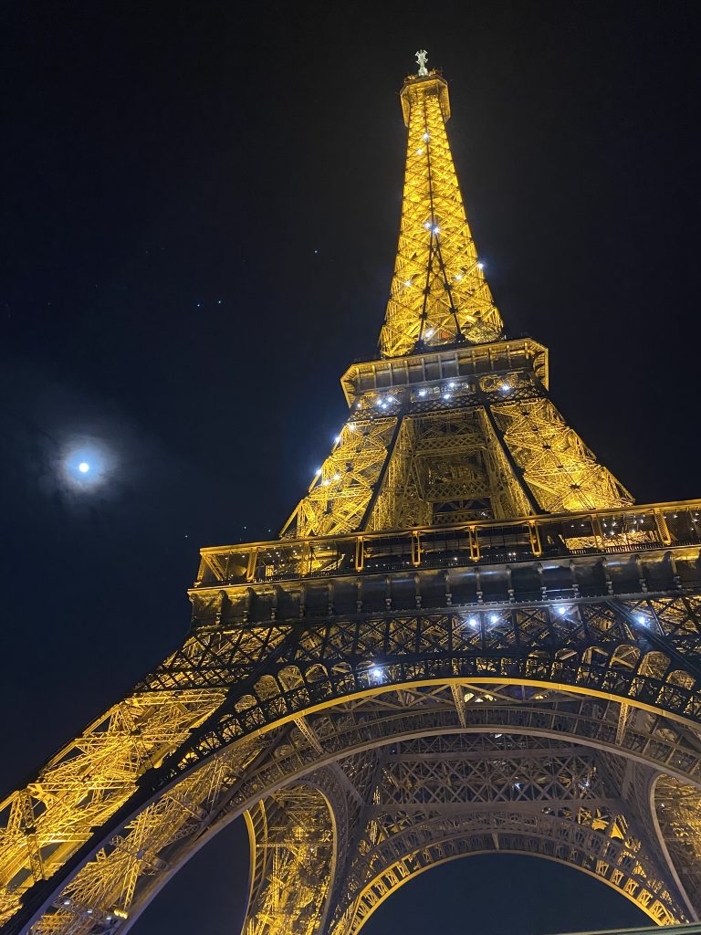 Eiffel Tower sparkling at night with a full moon in the background as seen on a Christmas Light bus tour in Paris in December