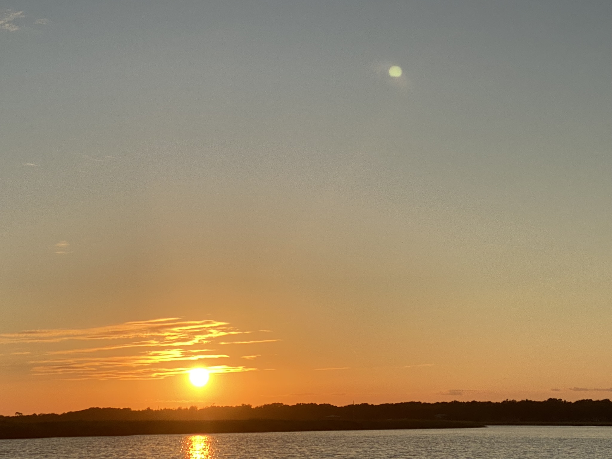 Sunset of Charleston bay. The sun is dipping behind the horizon illuminating the sky with beautiful colors. You can see land and water. Picture taken from a boat