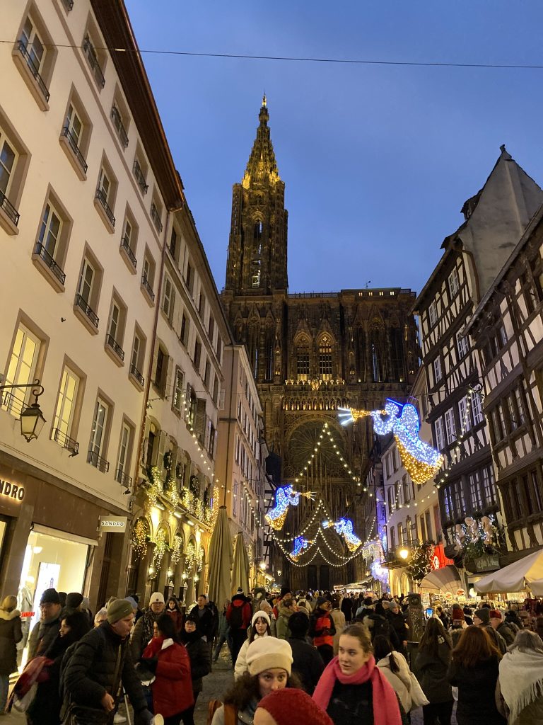 Strasboug city street with angel lights hung above the street and a church steeple in the background
