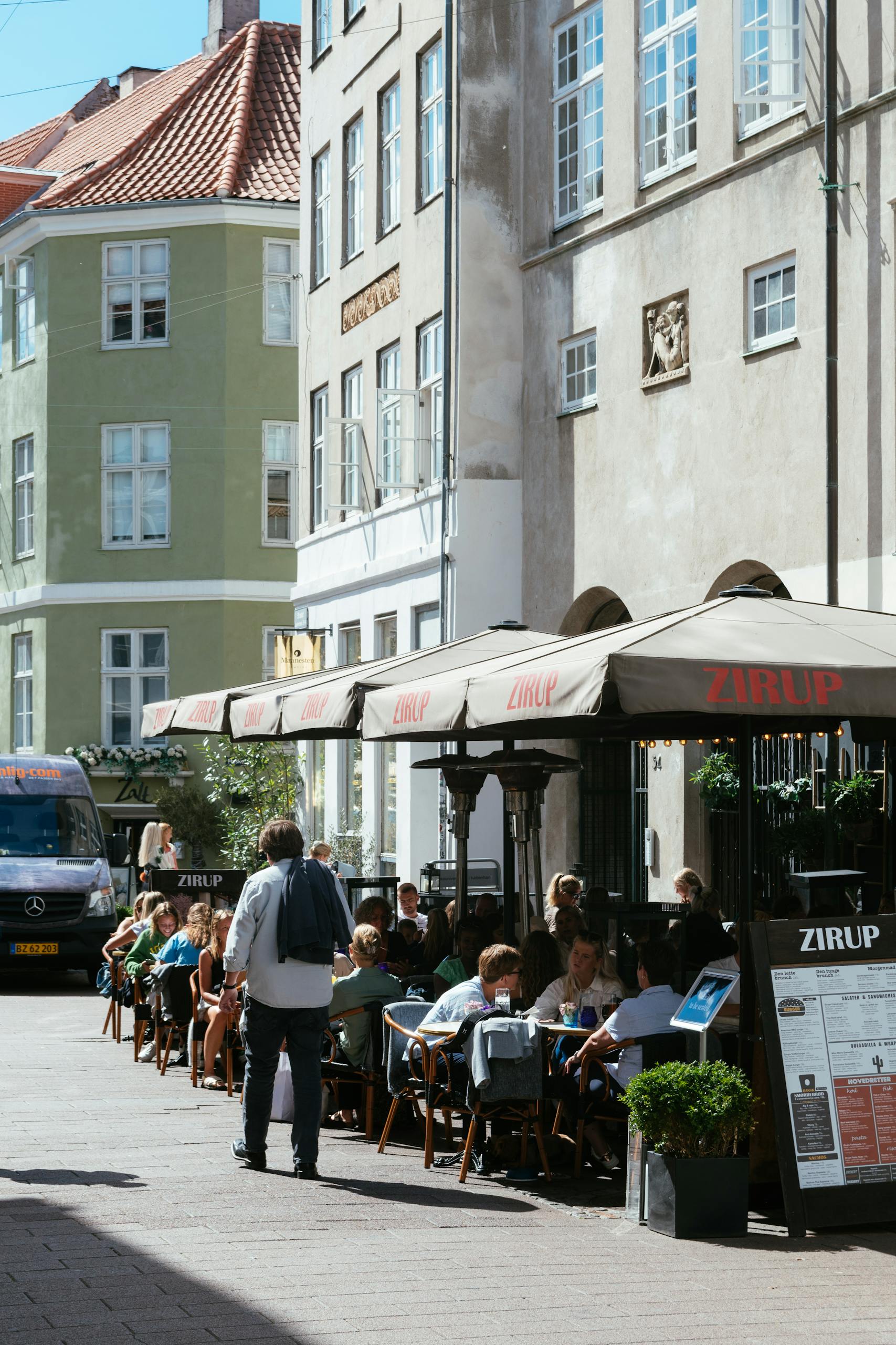 Outdoor dining at a bustling cafe on a cobblestone street in Copenhagen, Denmark.
