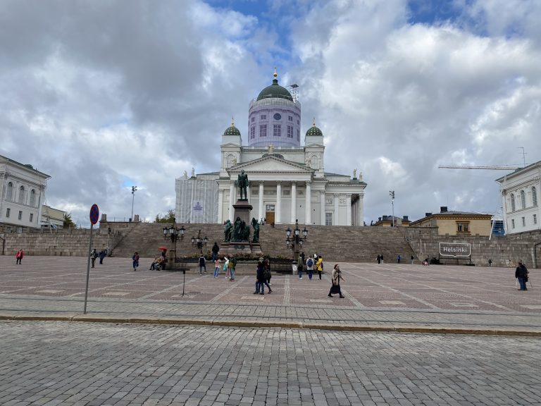 Hidden places in Helsinki large building with people walking in front of it on a partly cloudy autumn day