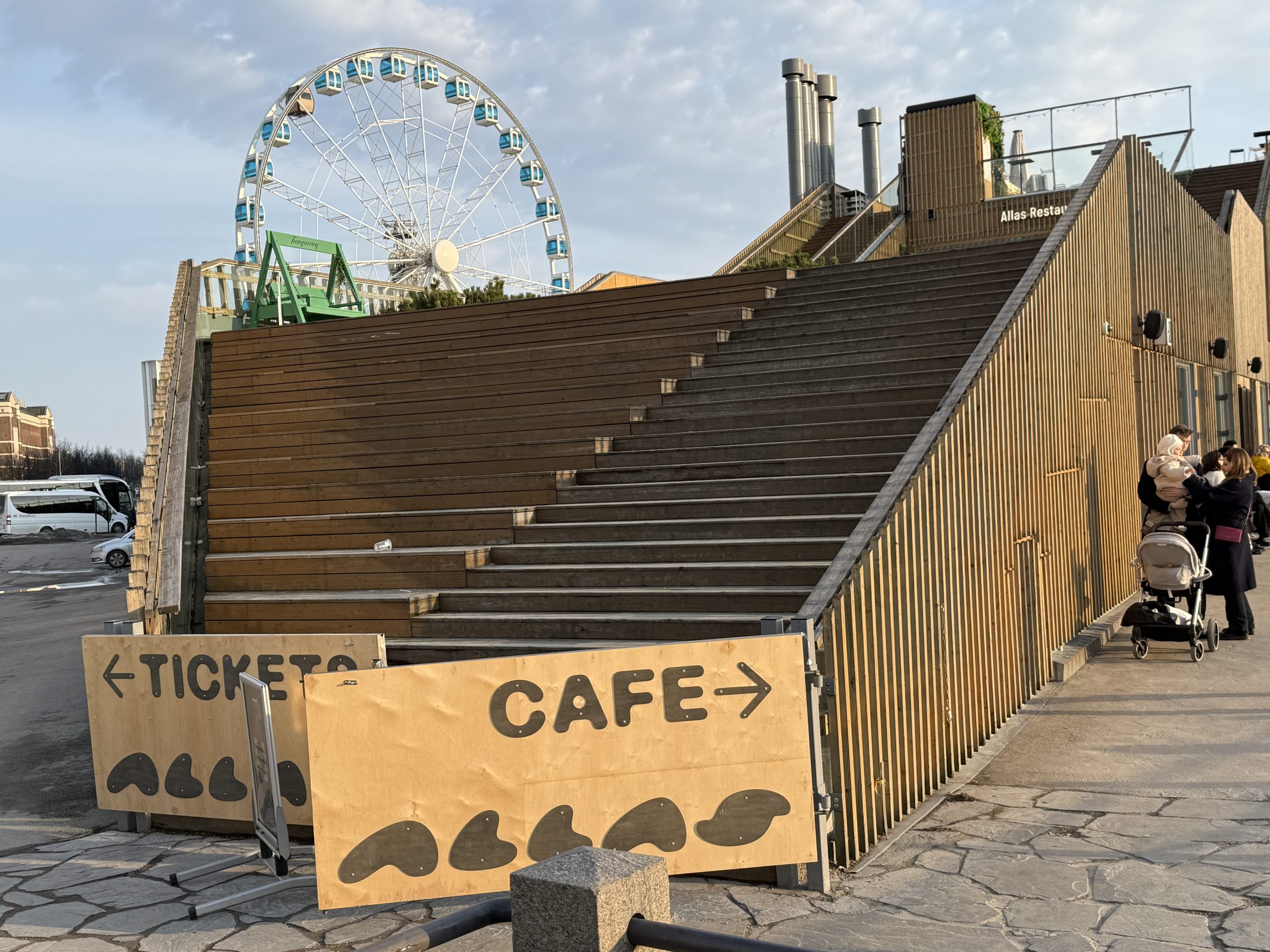 Entrance to the Alas Pool Sauna in the secret saunas of Helsinki, Finland as seen from the outside with a ferris wheel in the background as well as a sign pointing to the cafe and tickets
