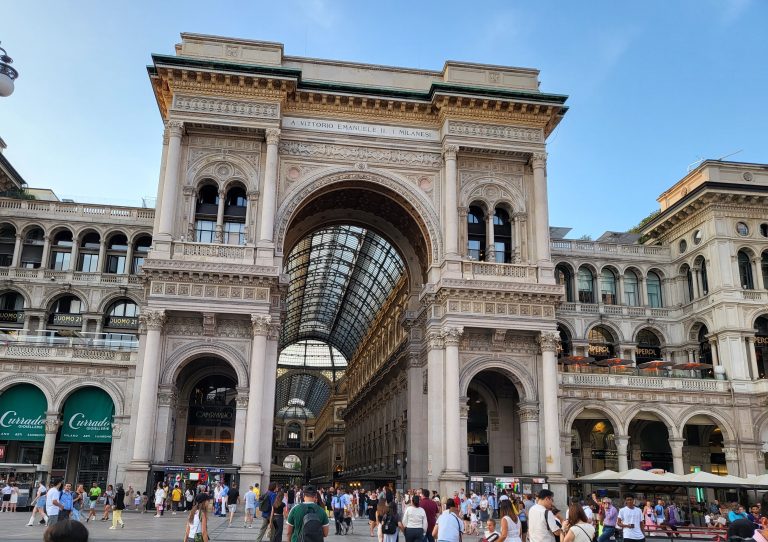Entrance to Galleria Vittorio Emanuele II in the Duomo plaza filled with people and shops