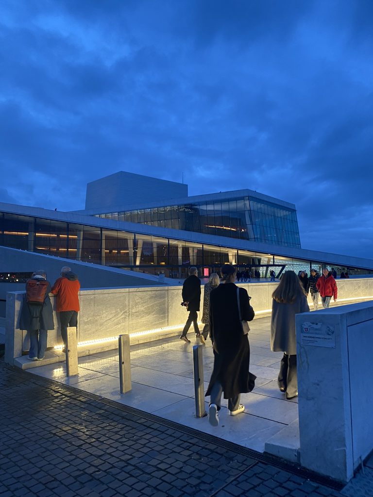 Evening time as you walk up to the Opera house a romantic spots in Oslo. You can see other people walking in front of you and the walk way lit up.