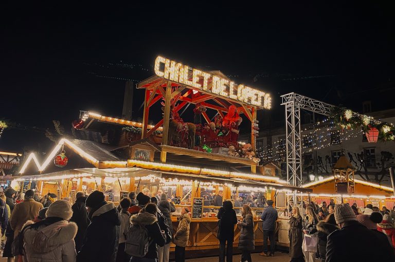 Strasbourg Christmas Market entrance to Chalet de Lopeta. The market is crowded with people, vendor stalls and Christmas lights