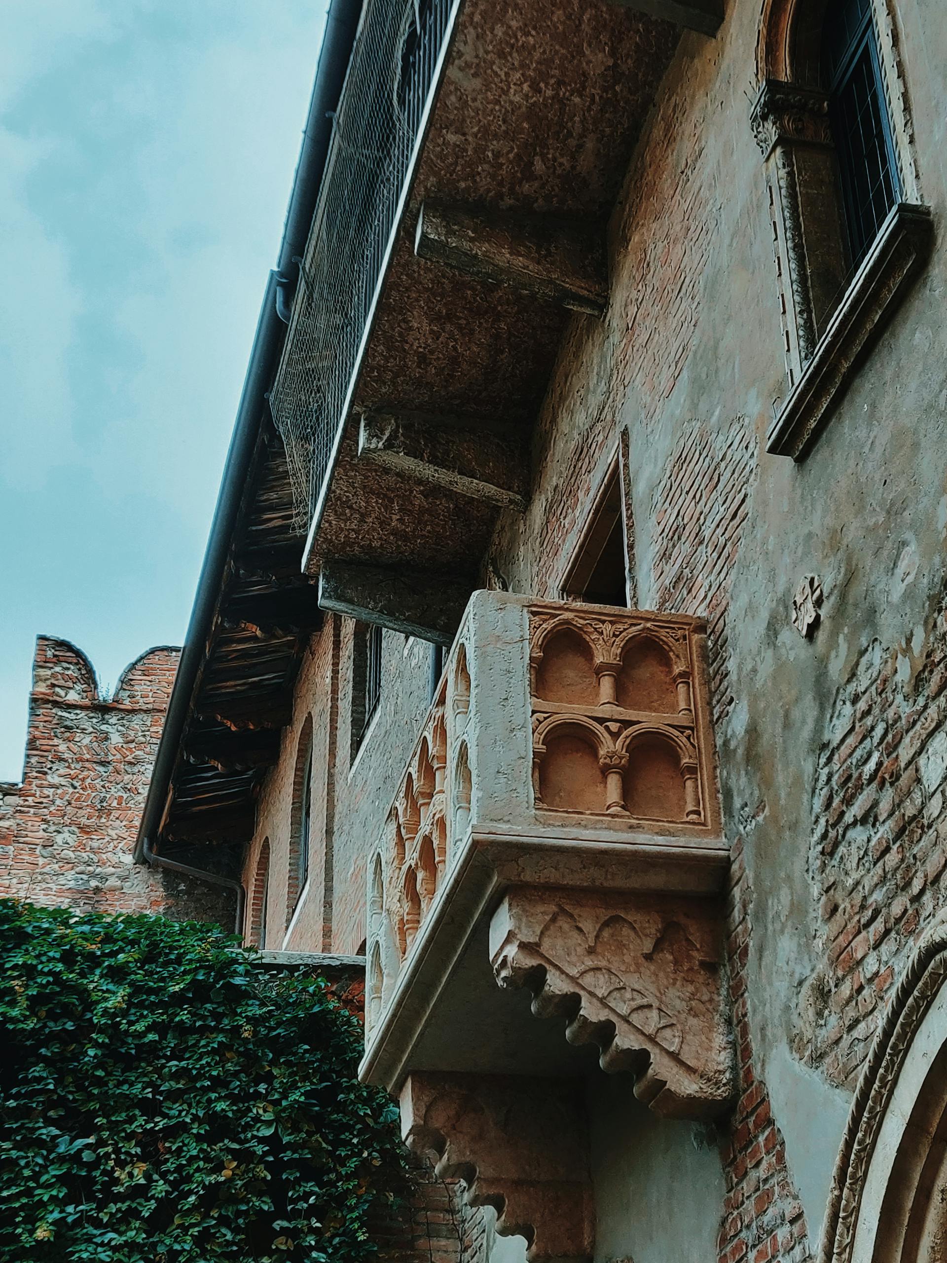 A low-angle view of an old stone balcony on a historic brick building exterior that is Juliet's balcony in verona, Italy