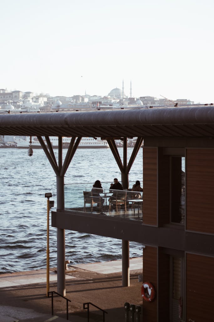 A serene view of waterfront dining with an urban background and a few people enjoying the day.