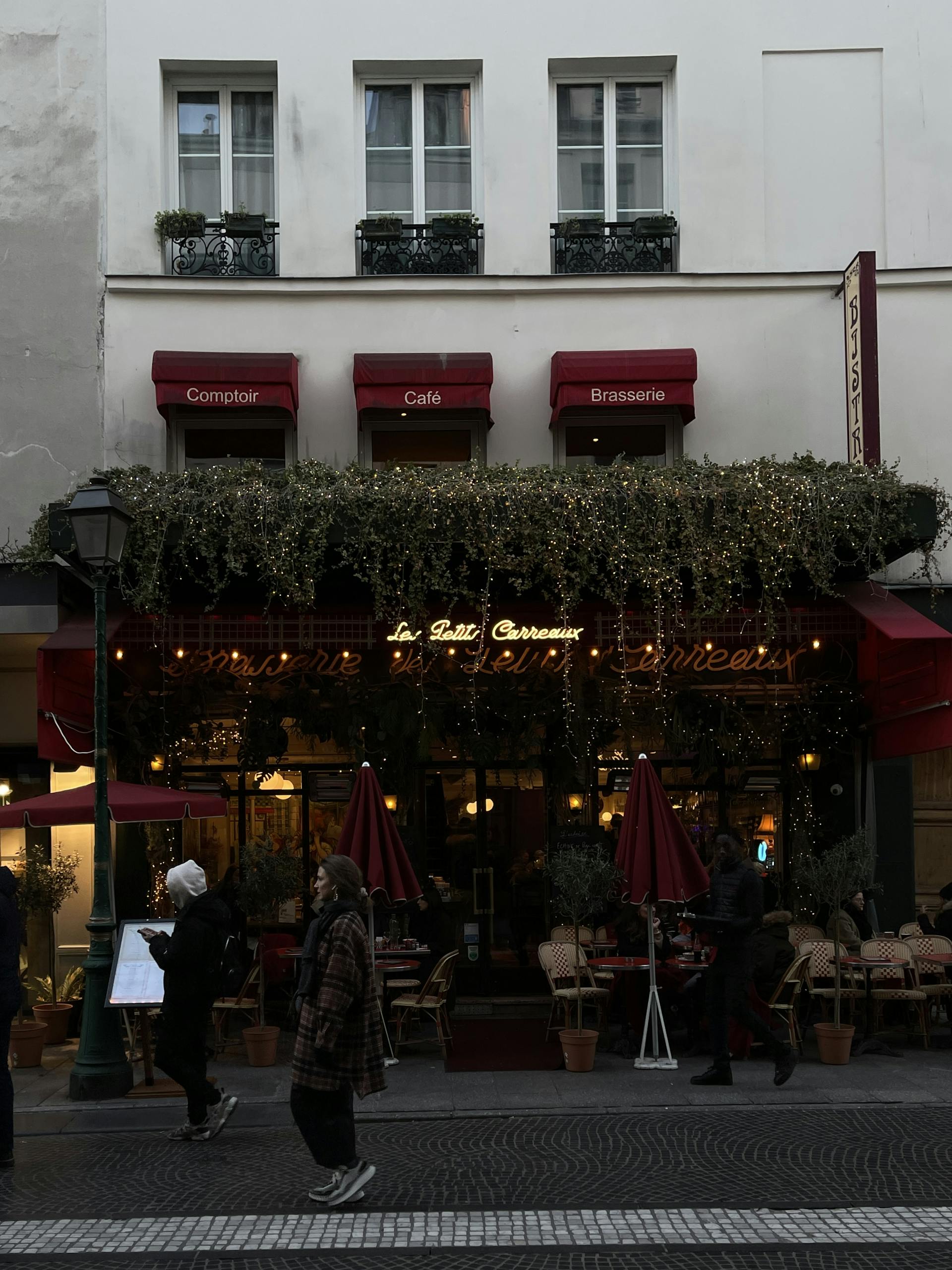 Discover a charming Parisian cafe with a lush ivy facade, people strolling by, and warm ambient lighting.