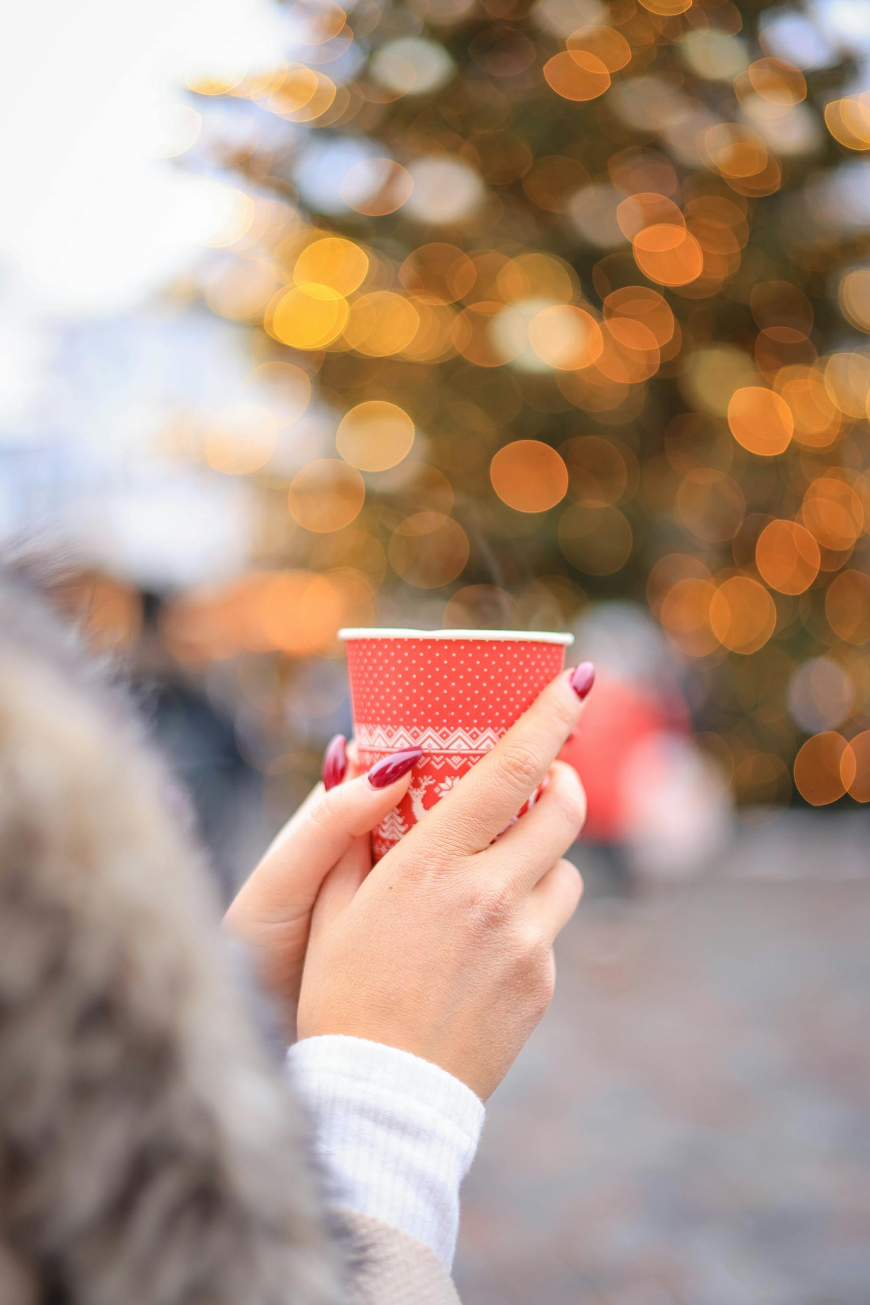 Hands holding a festive cup with a bokeh background, creating a cozy winter atmosphere.