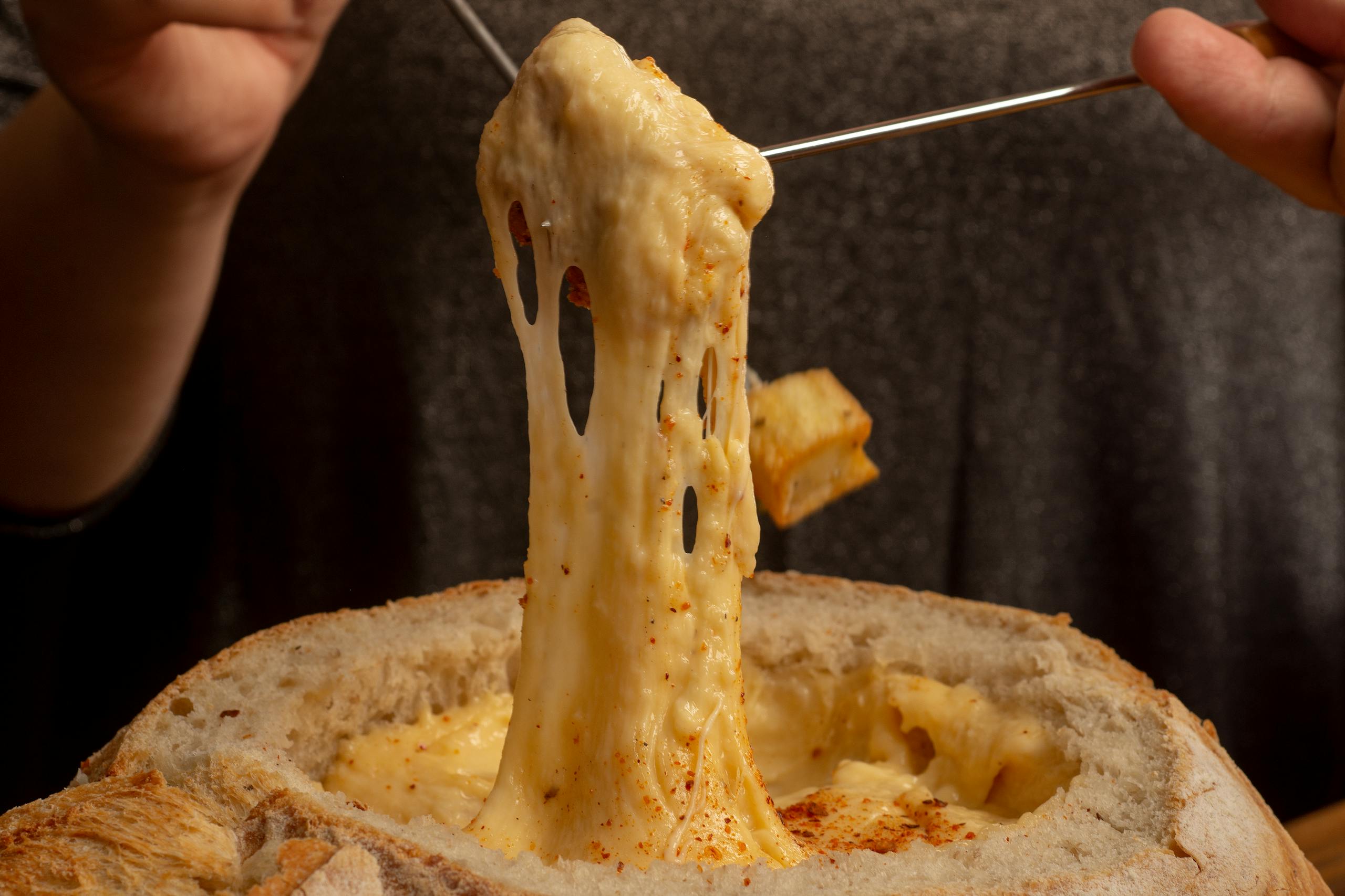Mouthwatering close-up of gooey melted cheese fondue being stretched from a bread bowl.