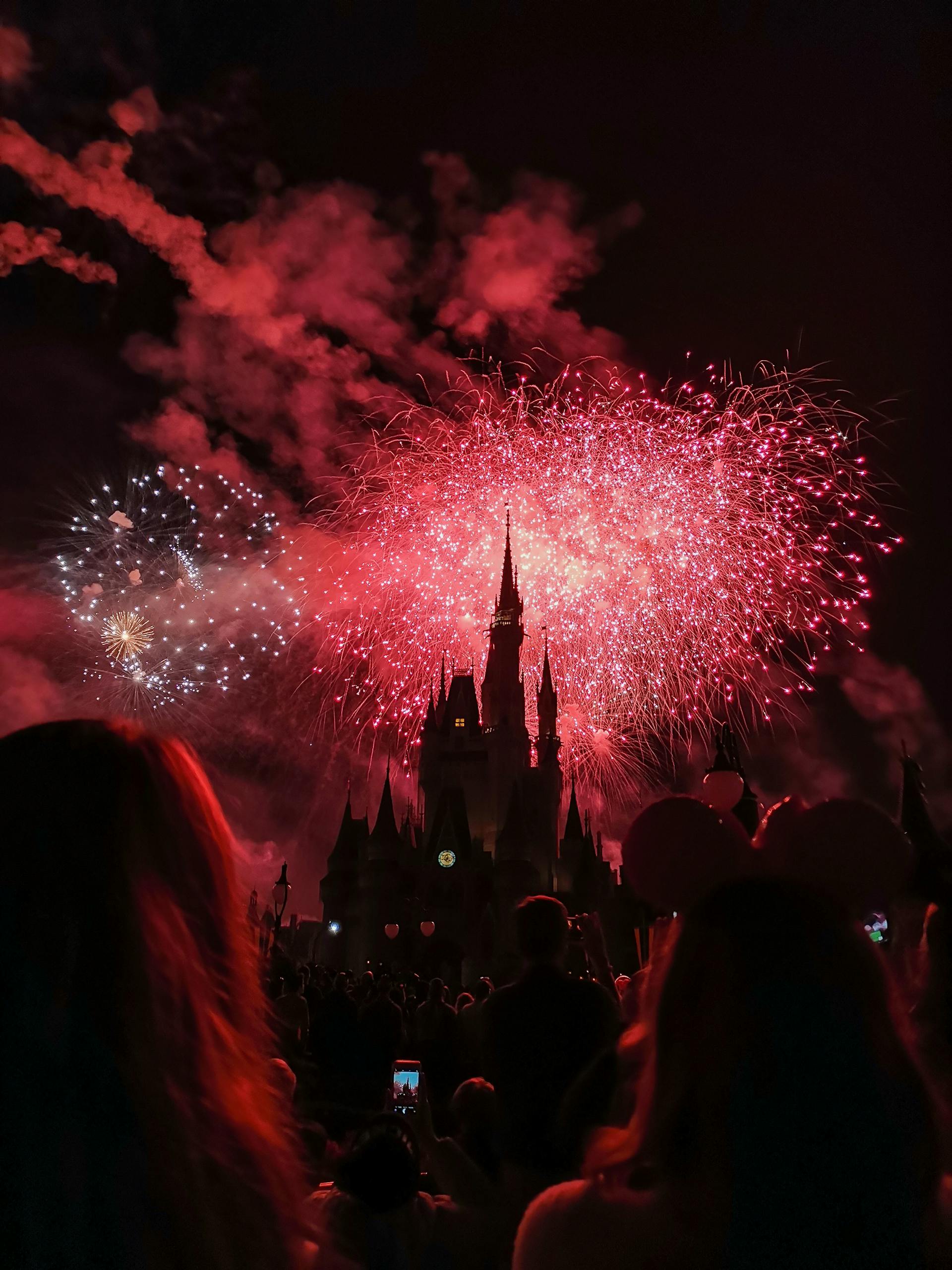 Vibrant nighttime fireworks explode over Disney castle, capturing a festive celebration with silhouetted spectators.