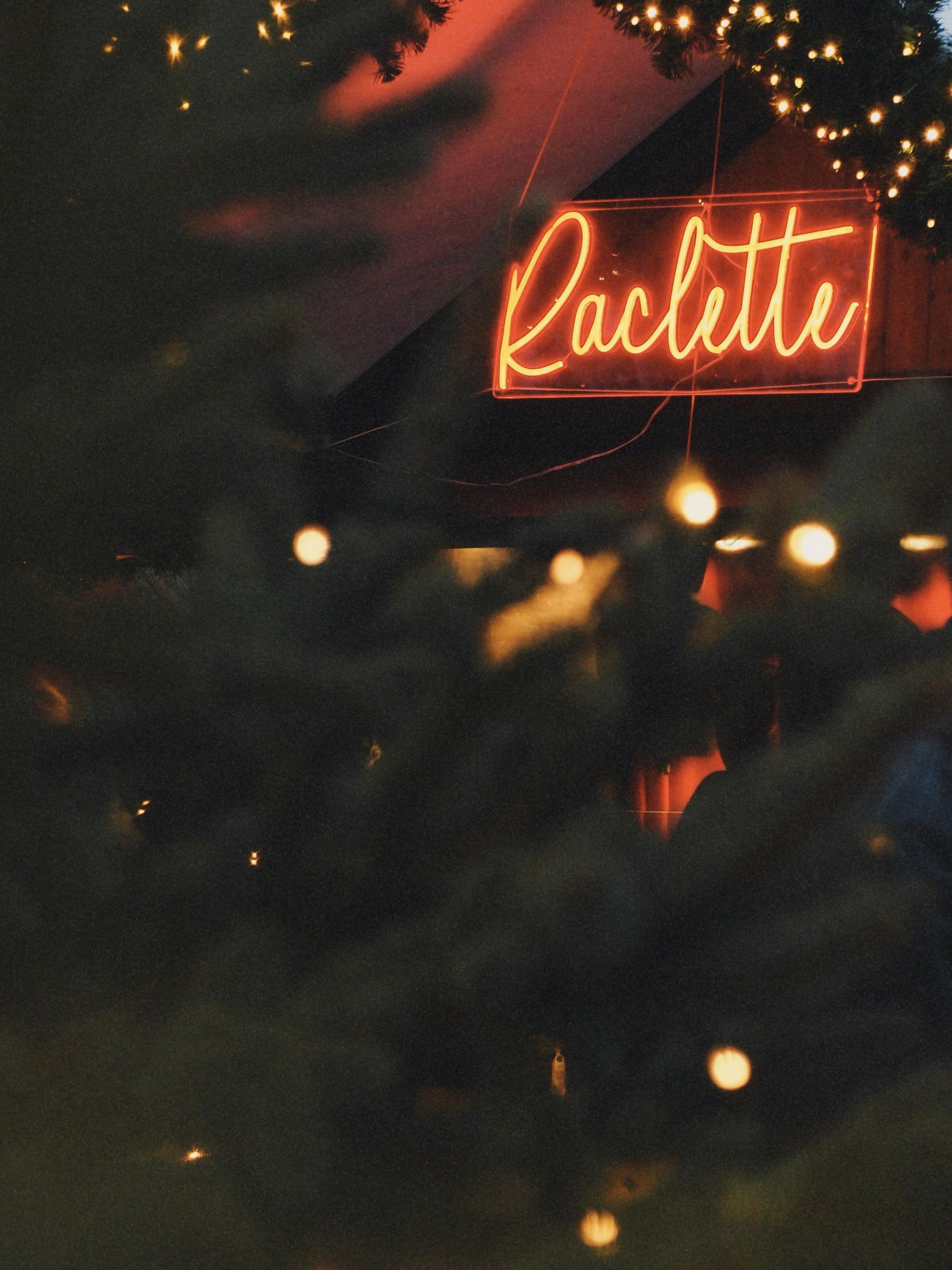 Warm festive lights and a Raclette sign at a Christmas market in Paris