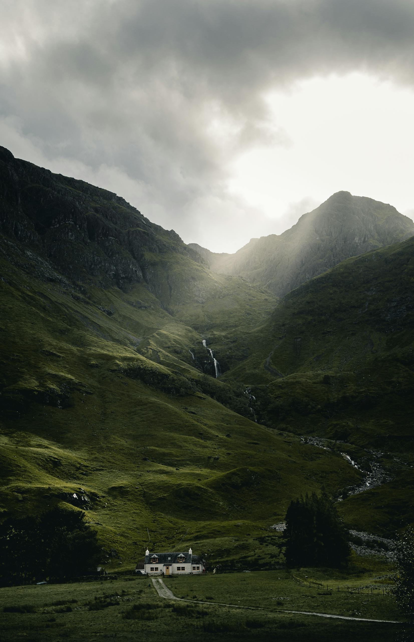 Breathtaking view of a cottage nestled in lush green Scottish highlands under dramatic, cloudy skies in best day trips from Edinburgh