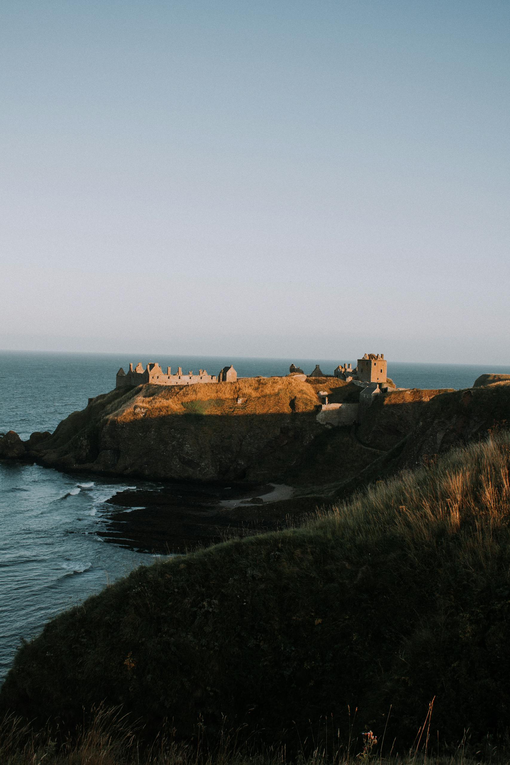 Breathtaking view of Dunnottar Castle perched on a coastal cliff with the ocean in the background during sunset in the best day trips from Edinburgh