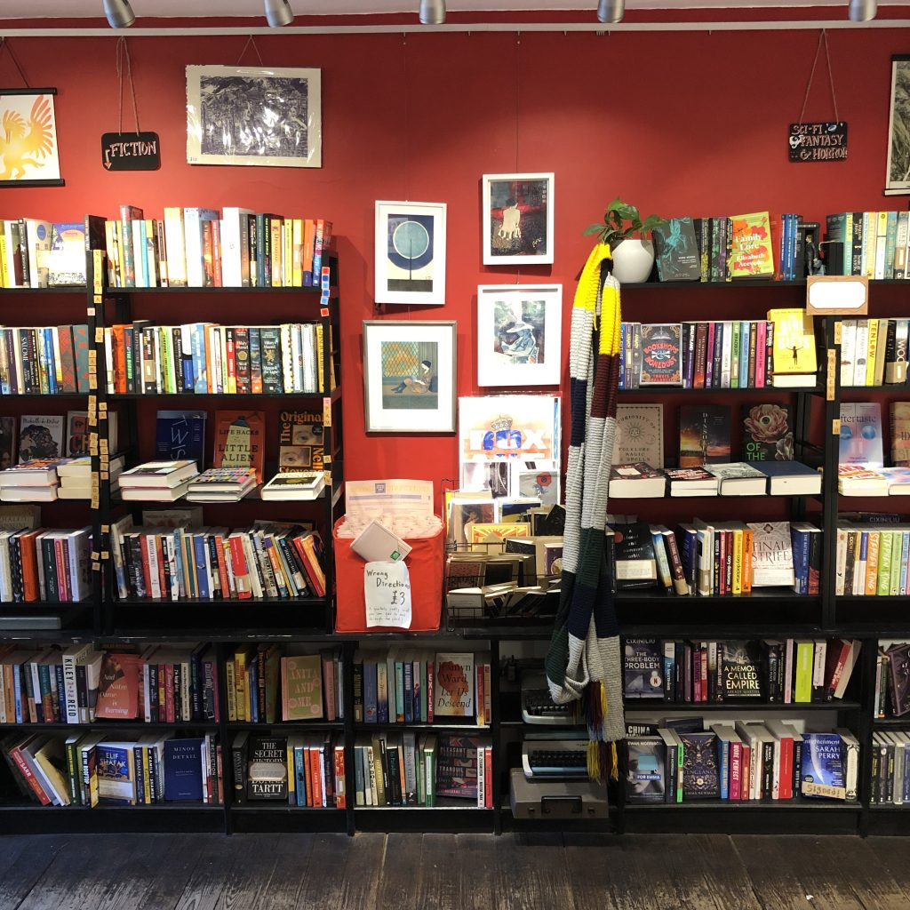 An inside photo of Typewronger Books in Edinburgh. Against a red wall you see shelves of books in a unique setting