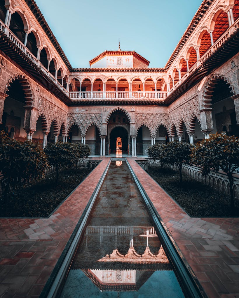 Majestic Alcazar of Seville courtyard with elegant arches and reflection during a vibrant sunset.