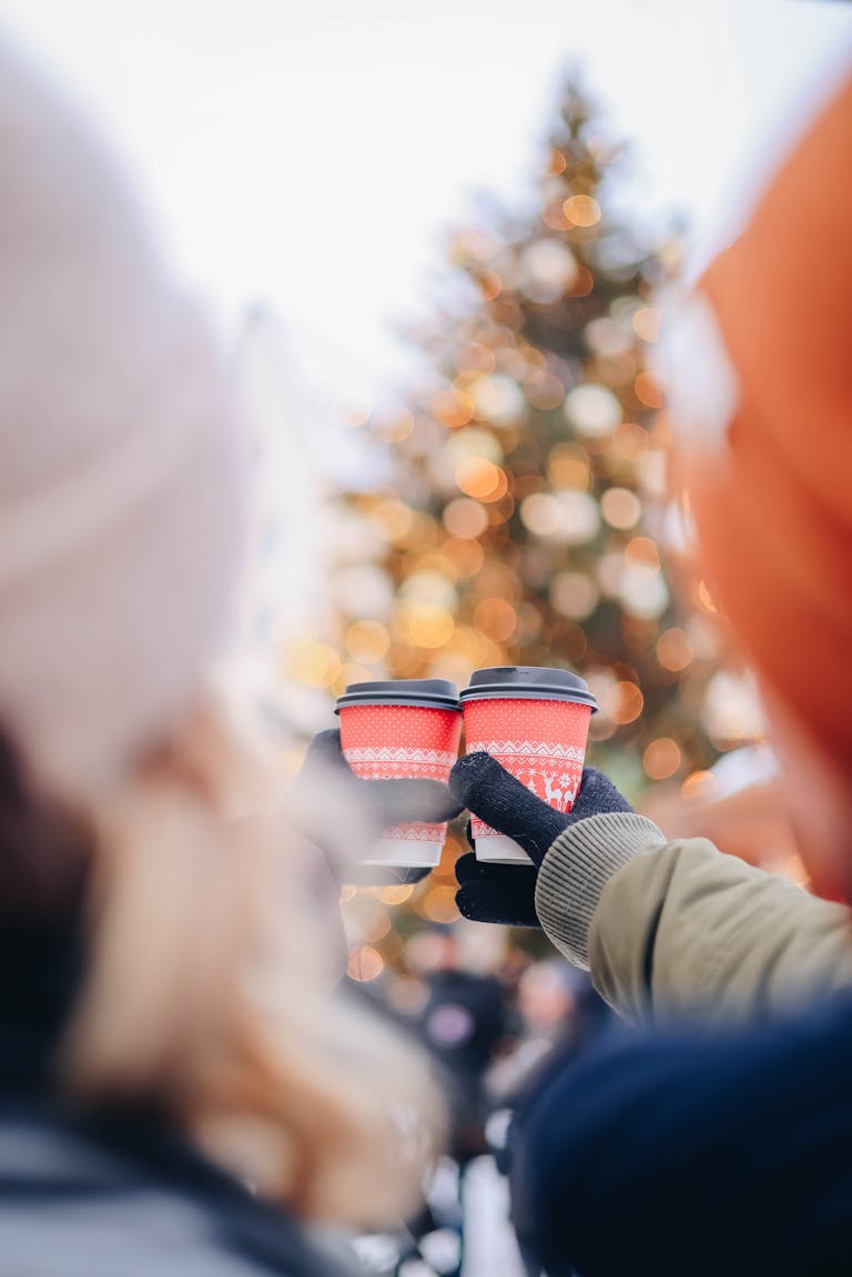 Couple holding festive coffee cups near a decorated Christmas tree in Christmas date ideas in Charleston, SC.