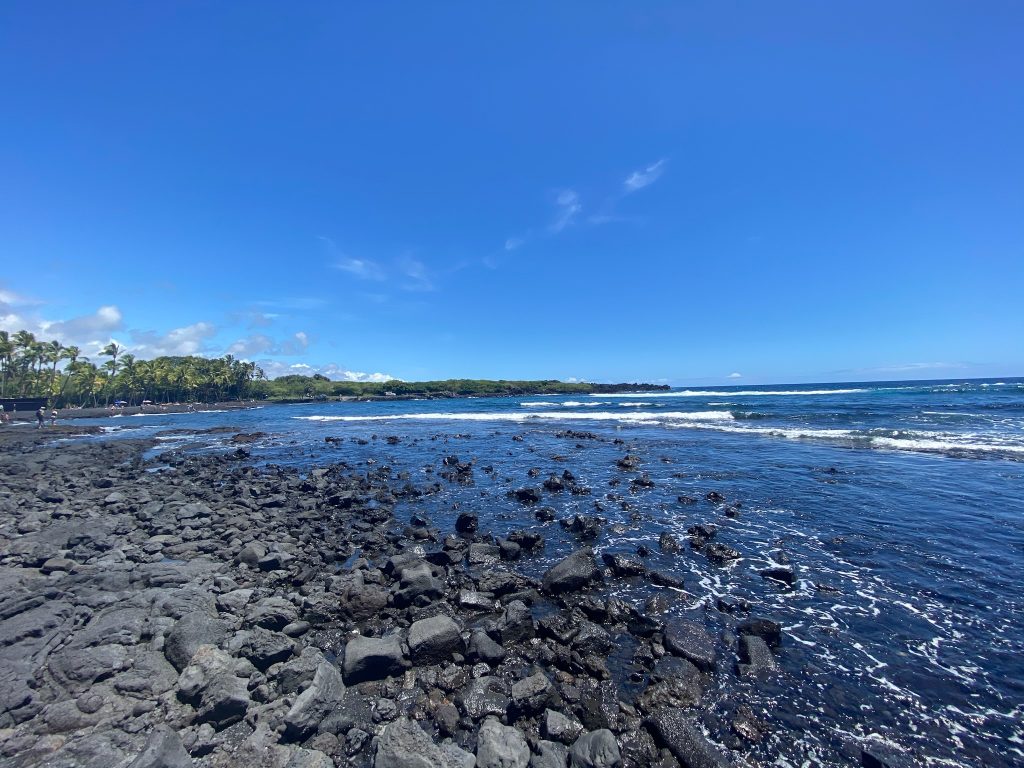 Black sand beach and blue water under a very blue sky in Hawai'i when looking at Maui vs the Big Island, Hawai'i