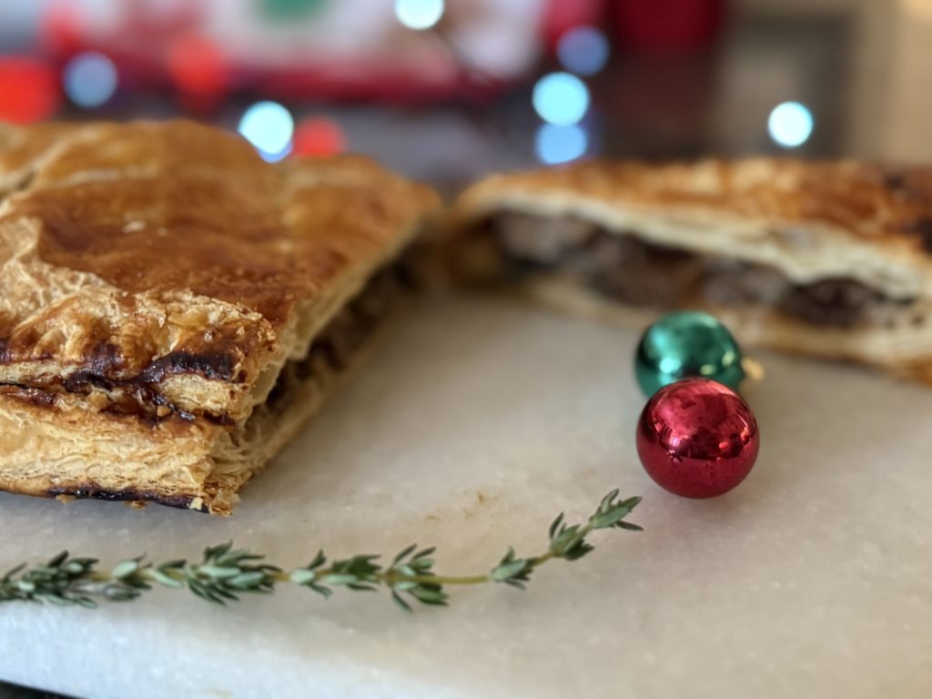 Mushroom Wellington with a slice cut adorned with thyme and Christmas ornaments for the holiday season