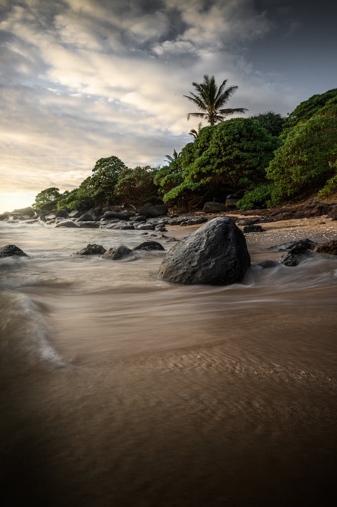 Beautiful tropical beach in Hawaii with palm trees and rocks during sunset, showcasing natural serenity when comparing Maui vs the Big Island