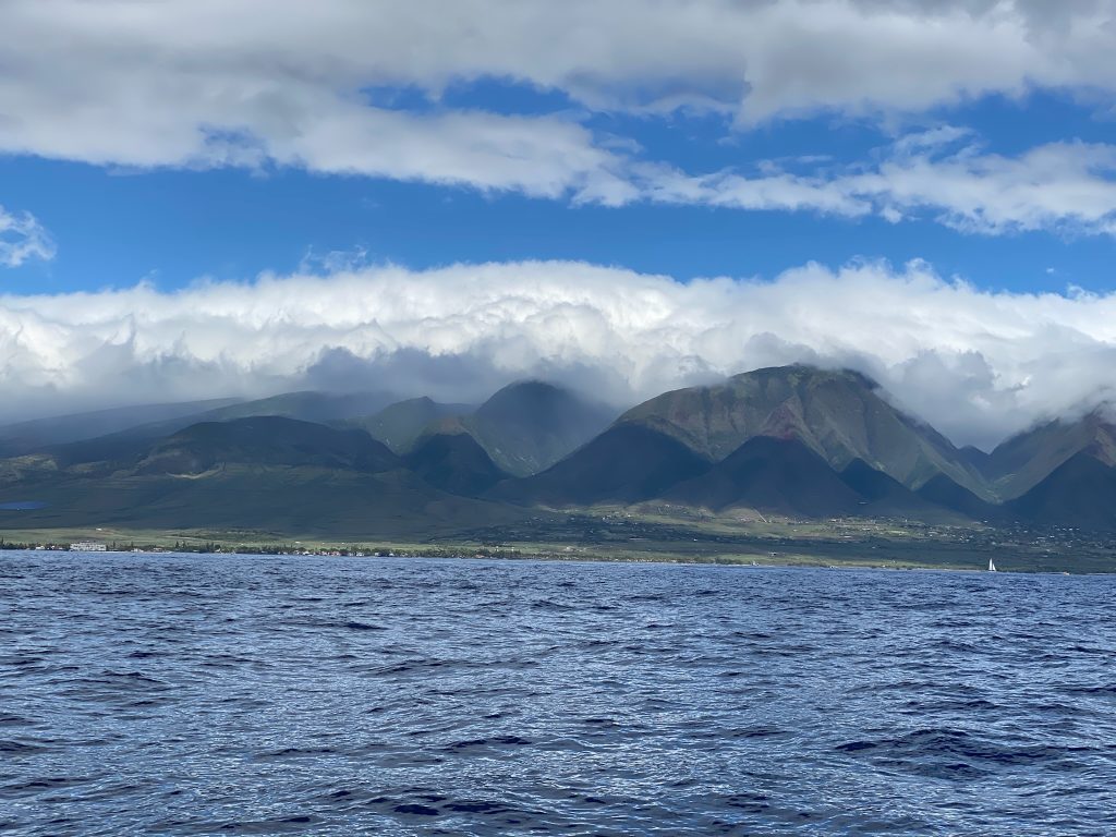 The lush green hilly landscape of Maui as seen from a boat in the water in Maui vs the Big Island, Hawai'i