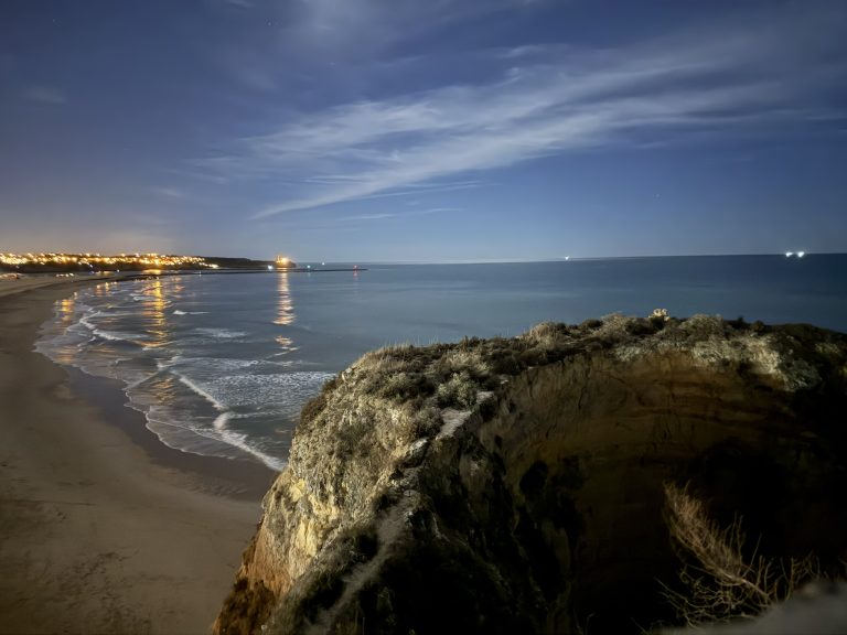 View from the end of a walk-out in the Algarve region of Portugal showing the beach and distant lights from buildings as well as part of a rock cliff as seen in how to plan a Lisbon-Algarve trip.