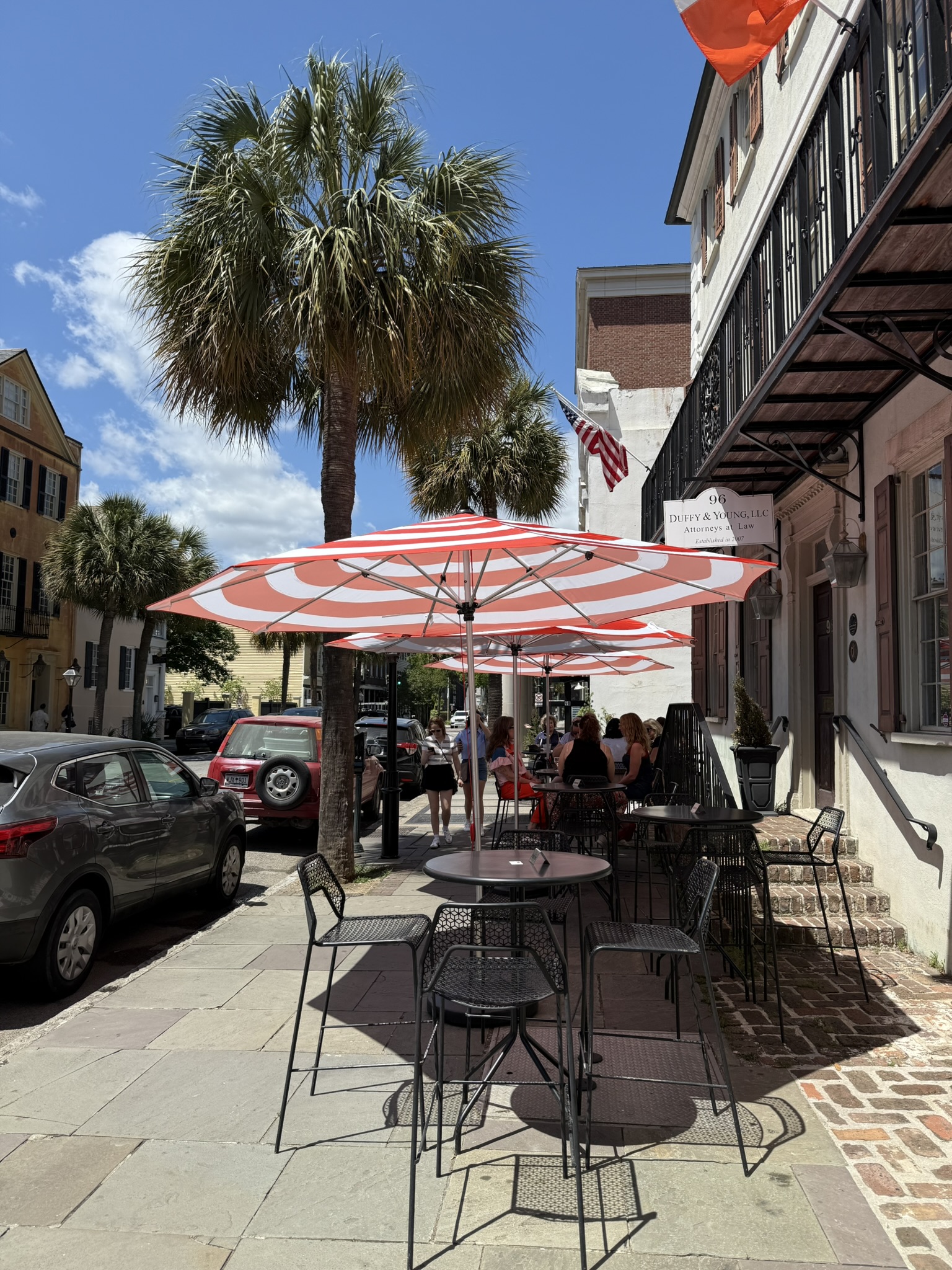 Umbrella covered table and chairs outside of a restaurant  on Broad St. in the summer in Charleston, SC in is Charleston worth visiting?