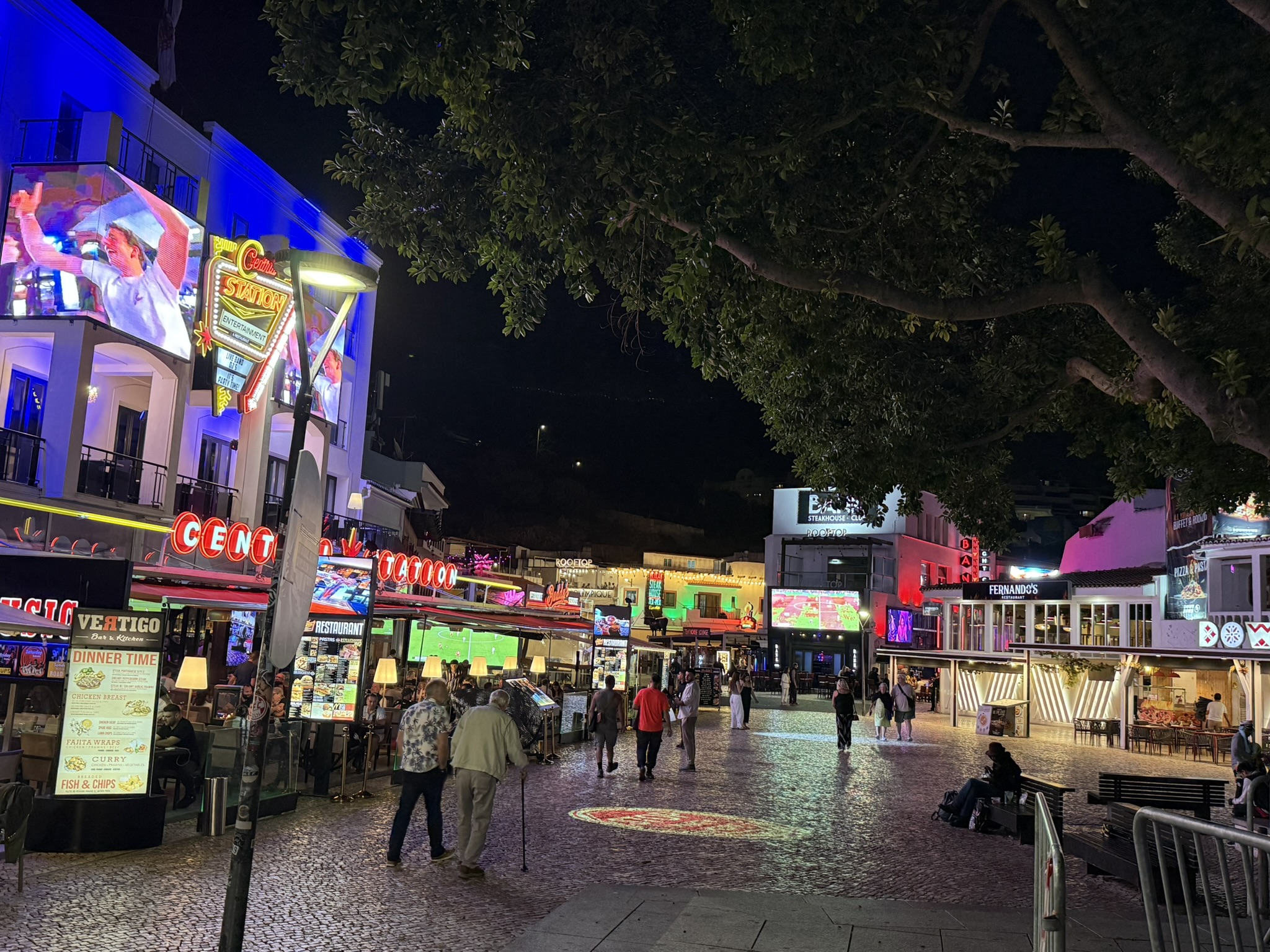 People of all ages walking down the street in Albuferia near  brightly lite restaurants and bars in spring break in the Algarve, Portugal