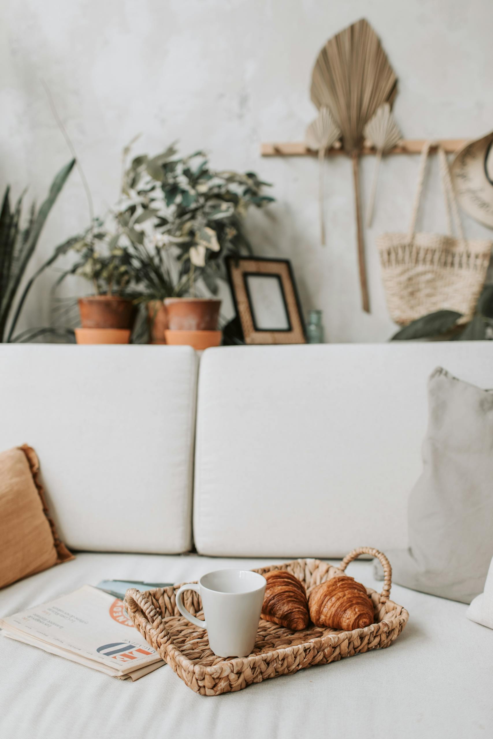 A cozy living room setup featuring coffee, croissants, and newspapers on a sofa.