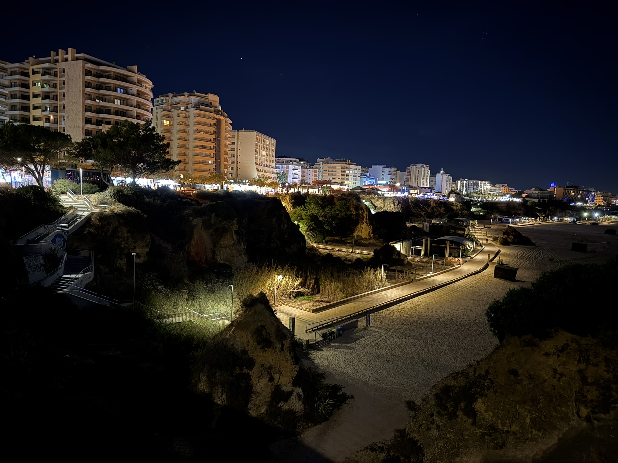 Hotels and restaurants lined up down the street above a beach as seen at night in the Algarve region of Portugal in best Algarve resorts