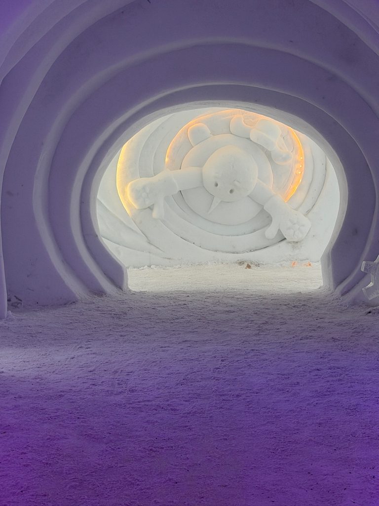 Entryway into Snowman World, where the walls and ceiling are built of snow and you can see a snowman sculpture coming out of the wall at the end of the hallway in travel guide to Lapland, Finland