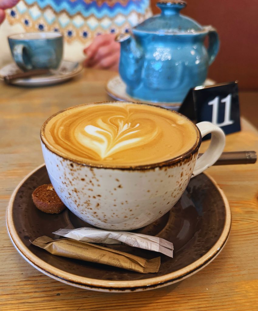 Cappuccino in a white and brown speckled mug with a blue ceramic tea pot in the background, as seen in 2 days in Tallinn itinerary