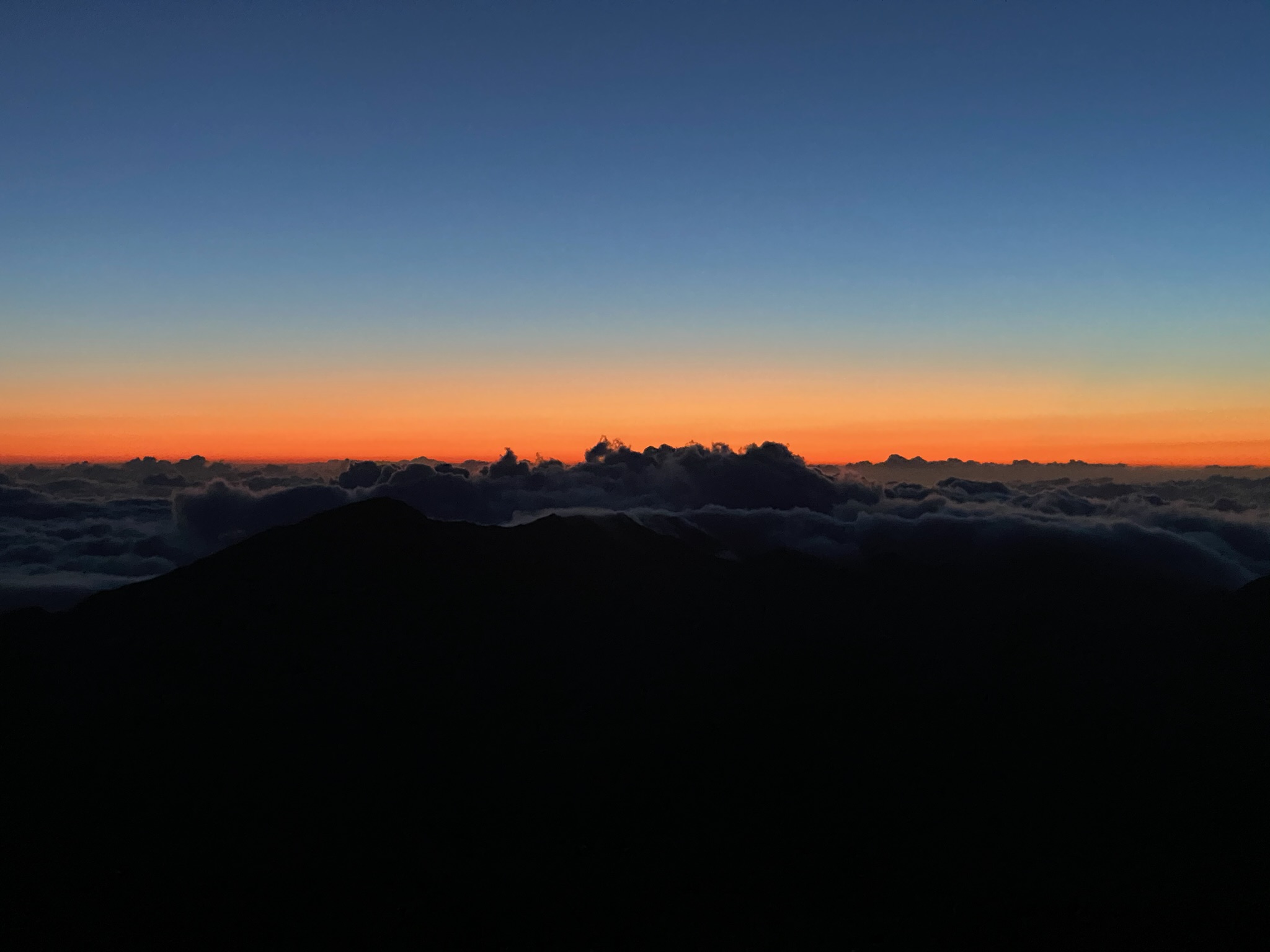 Beautiful oranges and blues in the sky above the clouds as we are watching the sunrise in Haleakalā National Park in the best things to do in Maui for couples