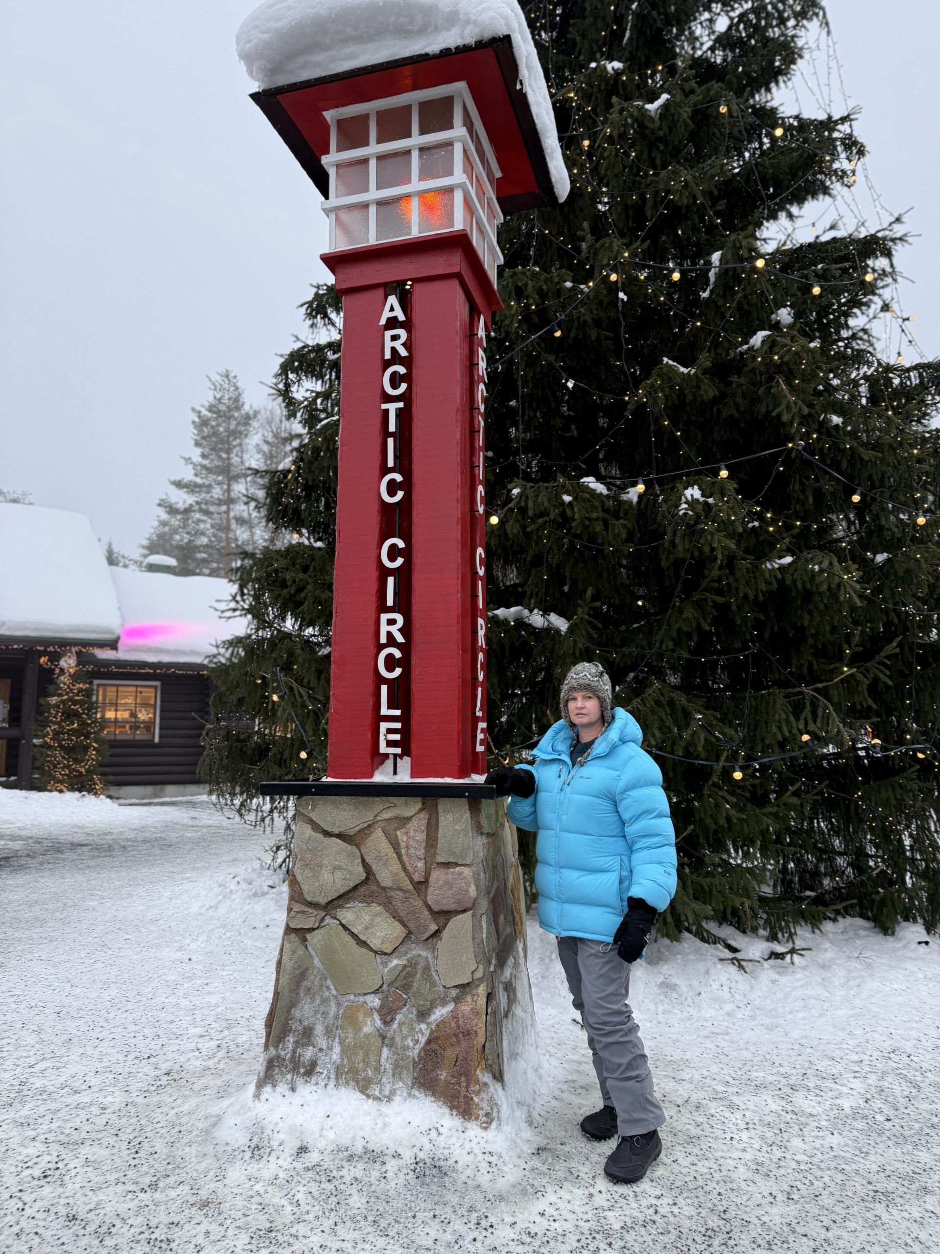 Casey Keller standing next to a post that marks the Arctic Circle in Santa Clause's Village in Rovaniemi, part of Lapland in Finland