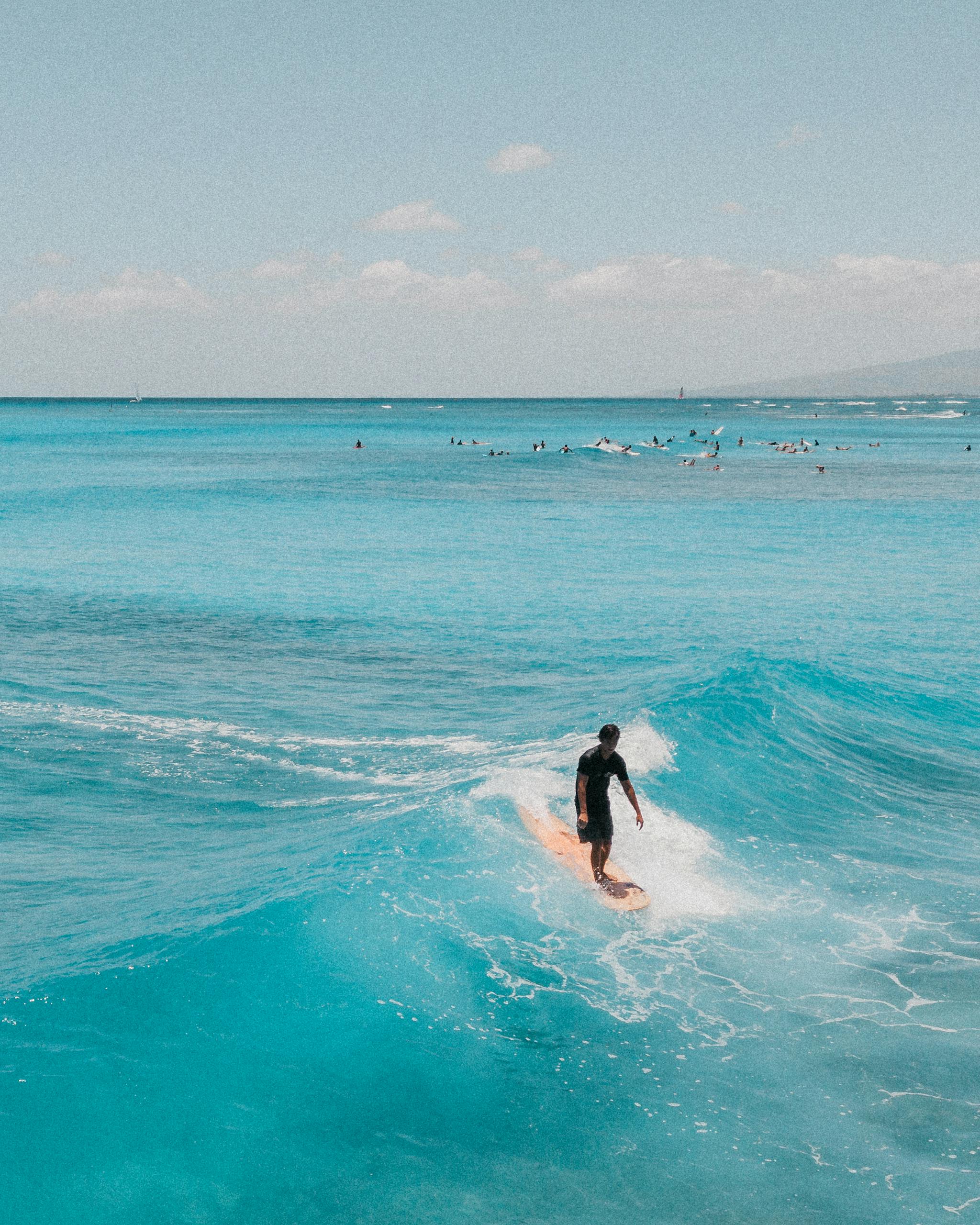 A surfer elegantly rides a wave in the clear blue ocean off the coast of Hawaii, capturing the essence of tropical adventure in the best things to do in Maui for couples