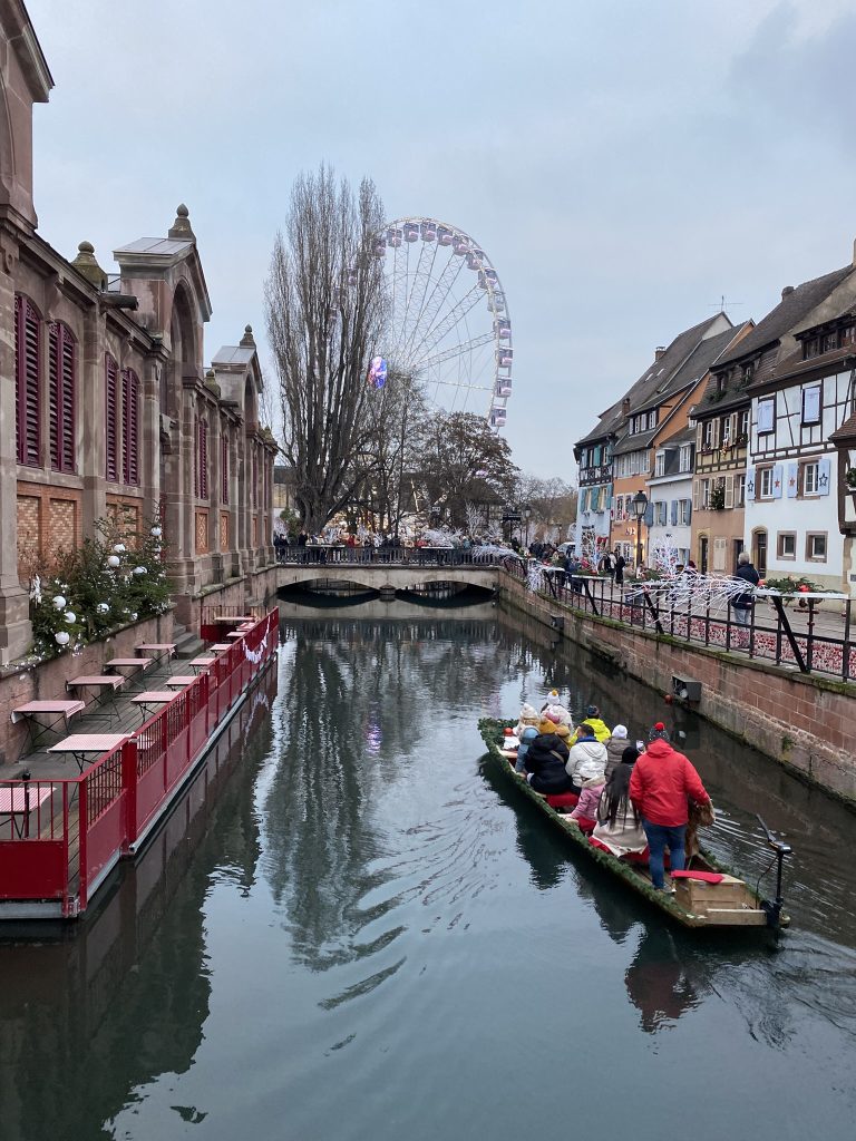 Small Venice in Colmar France during the December as seen in travel tips. A guide is taking people down the river in a small boat under a gray sky.