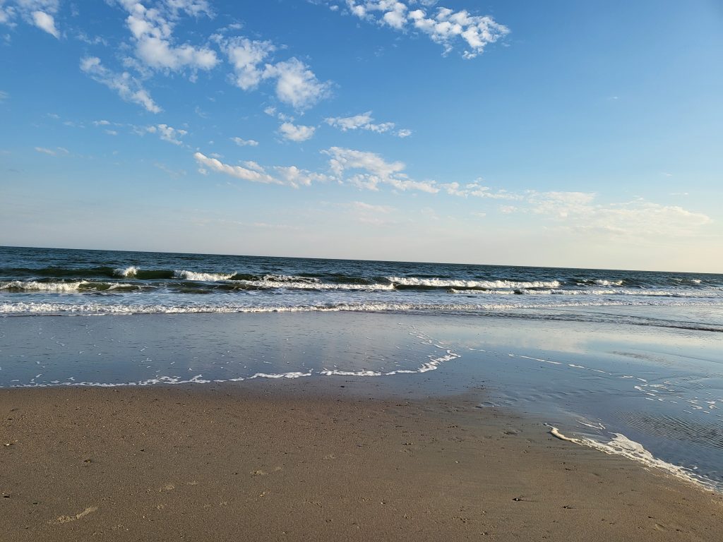 Beautiful view of the ocean from the Isle of Palms with the sun high in the sky the blue water and small waves and the sandy beach near Charleston, South Carolina