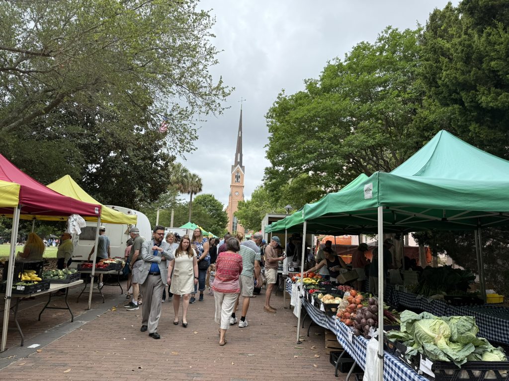 On a cloudy summer's day, tents over vendors booths align both sides of the walkways through Marion square. This is Charleston's Farmers Market.