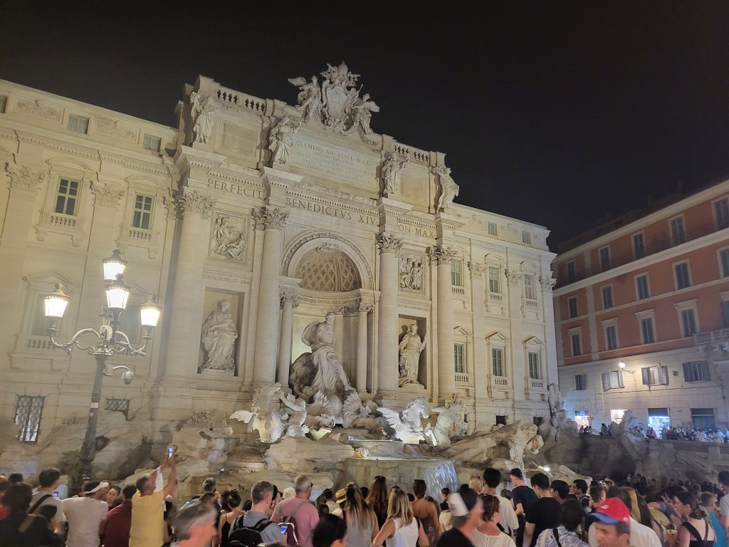 Trevi Fountain in Rome, Italy at night with a crowd of people in front of it taking photos.