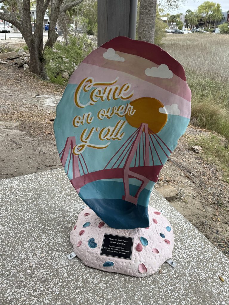 Giant Oyster statue/sign that is painted in colorful coastal colors with the Cooper River Bridge and Susnet on it. It reads, "Come on Over" on it.