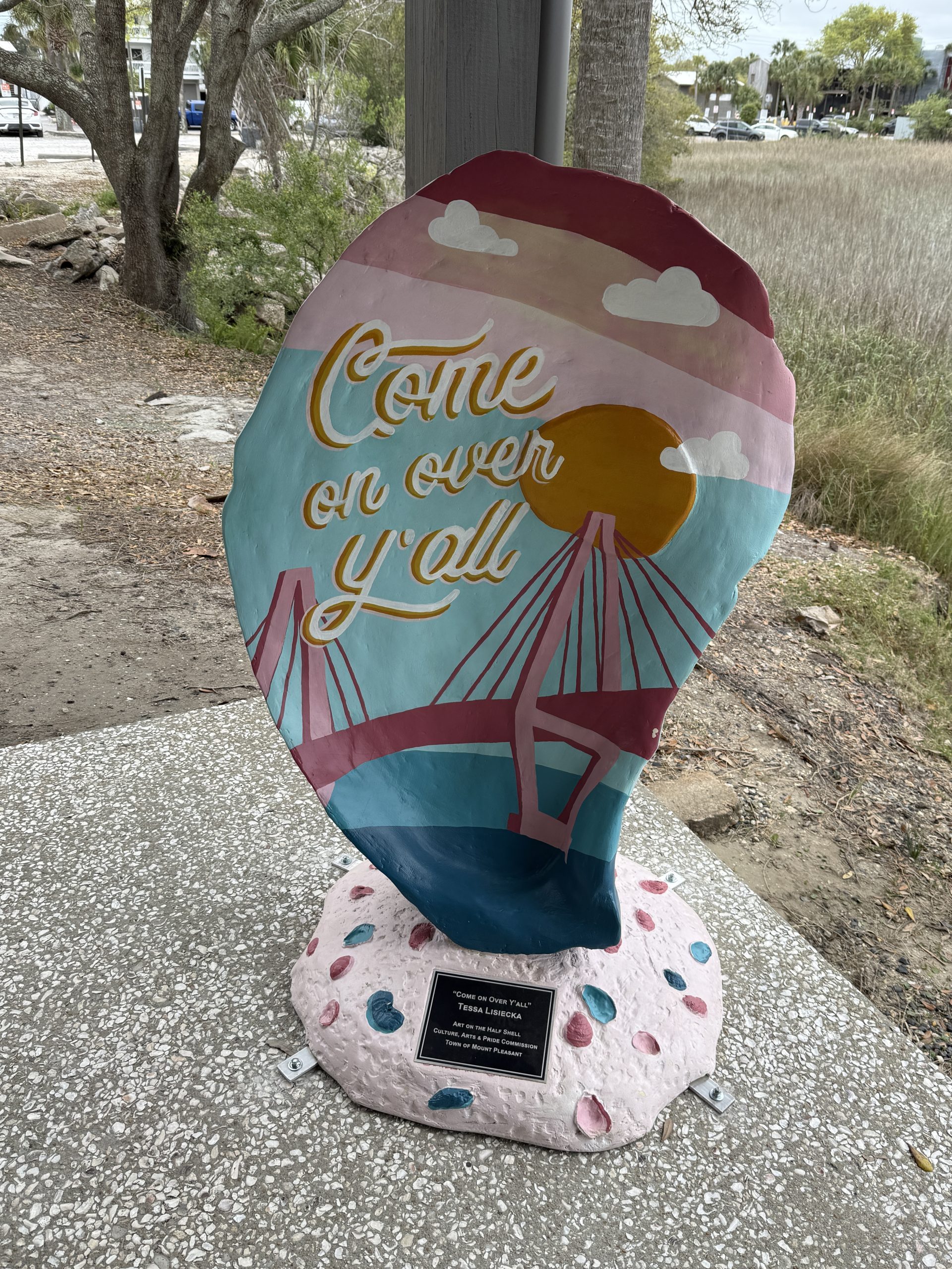 Giant Oyster statue/sign that is painted in colorful coastal colors with the Cooper River Bridge and Susnet on it. It reads, "Come on Over" on it.