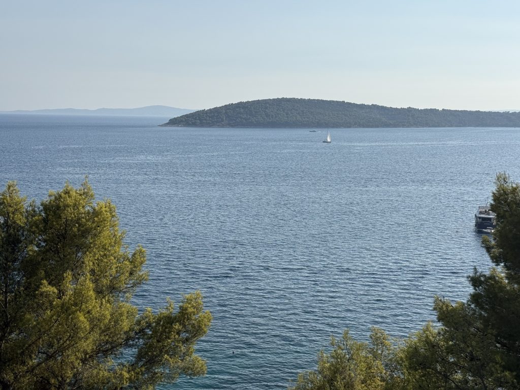 A lone sailboat crossing the blue Adriatic off Split, with a pine-covered island behind