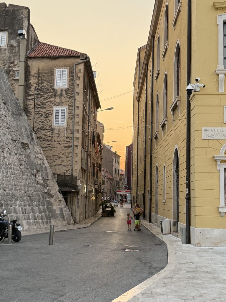 Narrow Old Town street glowing under a golden sunset sky beside the Croatian National Theatre in Split