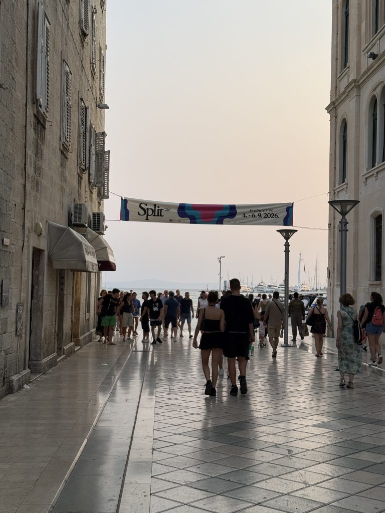 Narrow street in Split, Croatia's Old Town leading toward the waterfront, with a "Split '26 Prokurative" event banner overhead