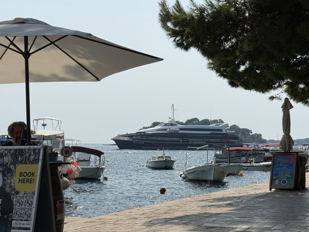 Krilo Eclipse catamaran pulling into Hvar Town's harbor, seen from the waterfront promenade
