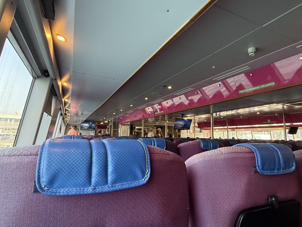 Blue and purple padded seats inside the Split to Hvar ferry cabin, with large windows and TV screens