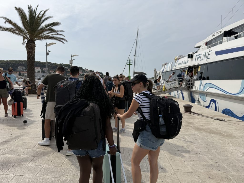 Travelers with suitcases and backpacks lining up to board a TP Line catamaran at Hvar Town's harbor