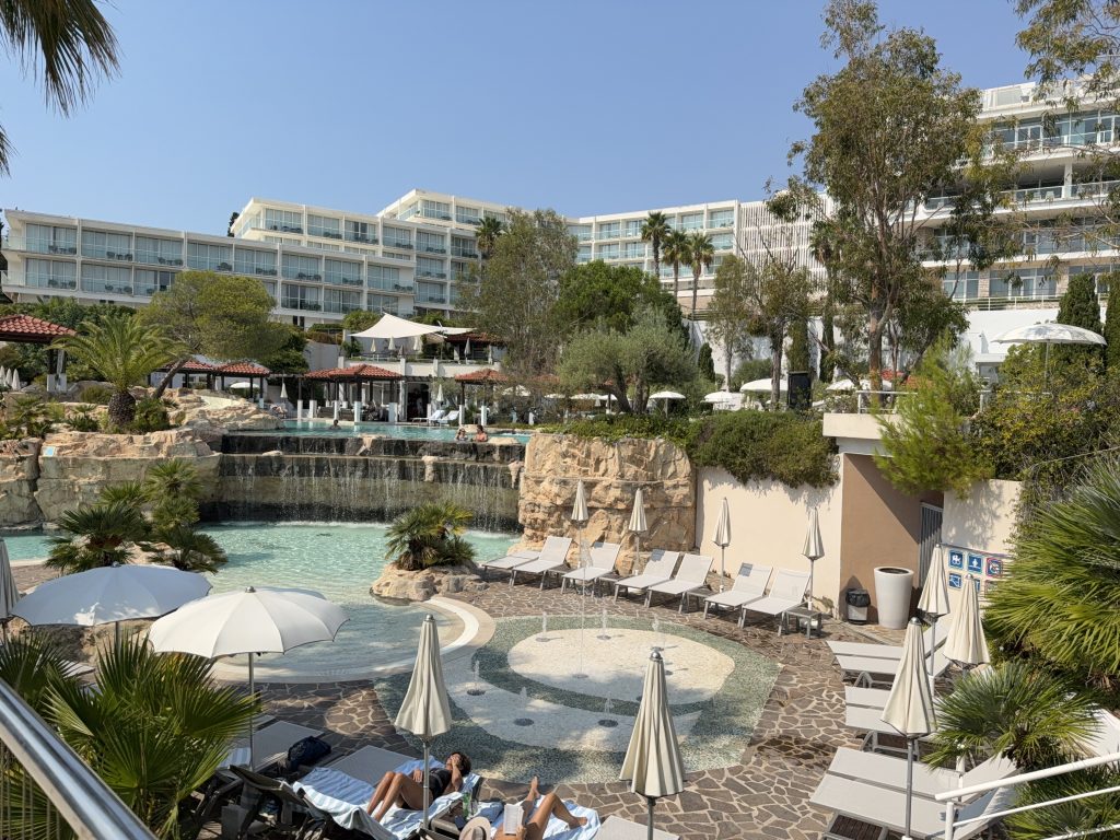 Tiered pools with rock waterfalls, a splash-pad fountain, and white sun loungers in the landscaped garden of Amfora Hvar Grand Beach Resort, Hvar Town