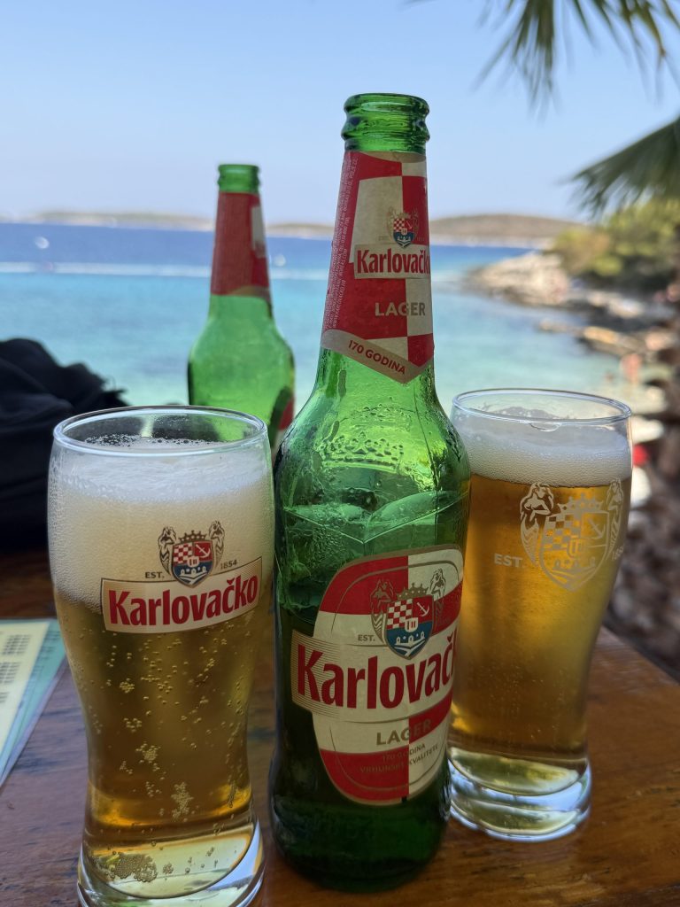 Turquoise water at Diamond Beach, Palmižana, Pakleni Islands near Hvar in the background of two Croatian beers at a beach bar
